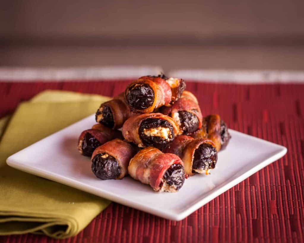 a white cocktail plate piled high with bacon wrapped prunes