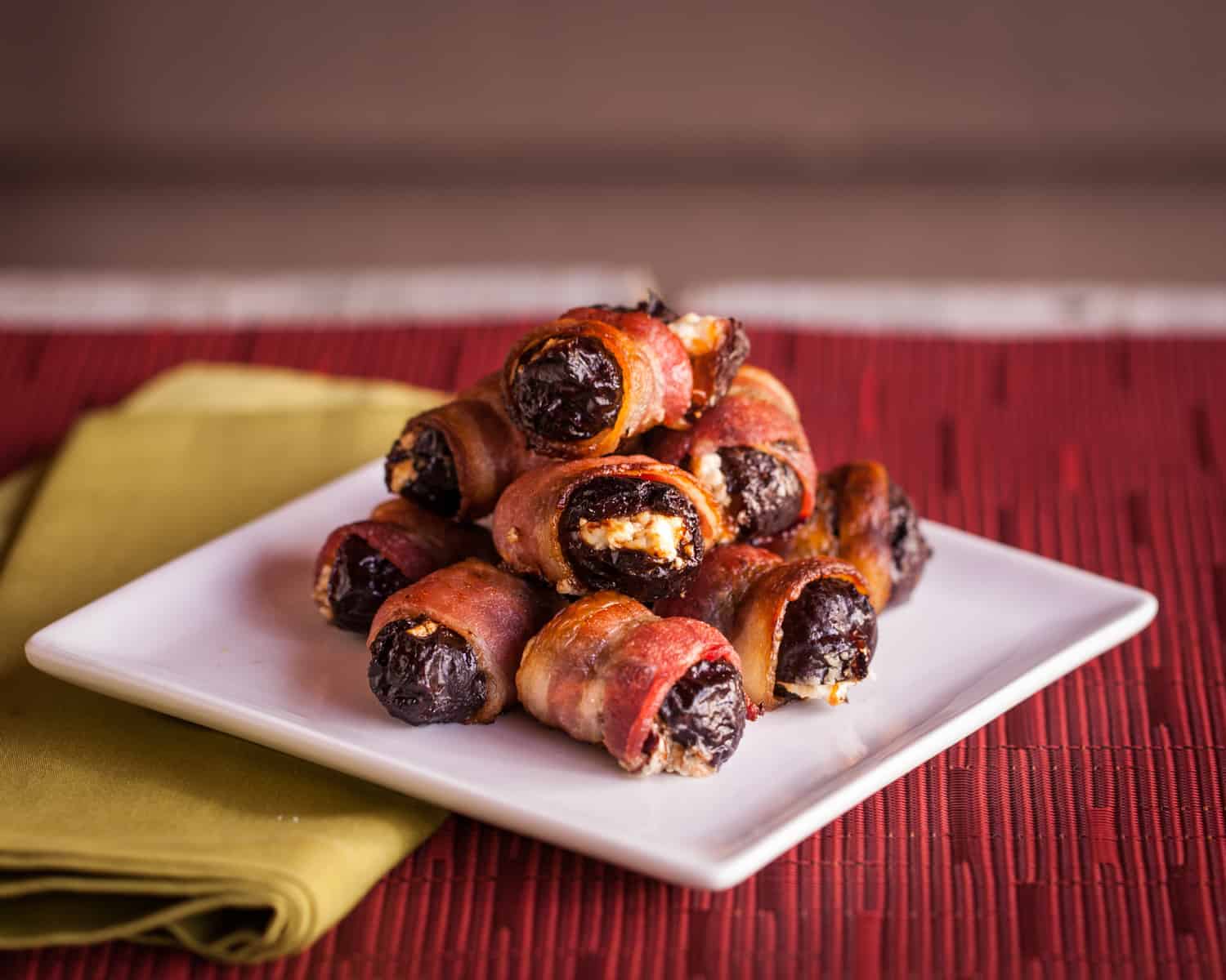 a white cocktail plate piled high with bacon wrapped prunes