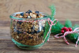 a bowl of Christmas granola with striped ribbon and greenery