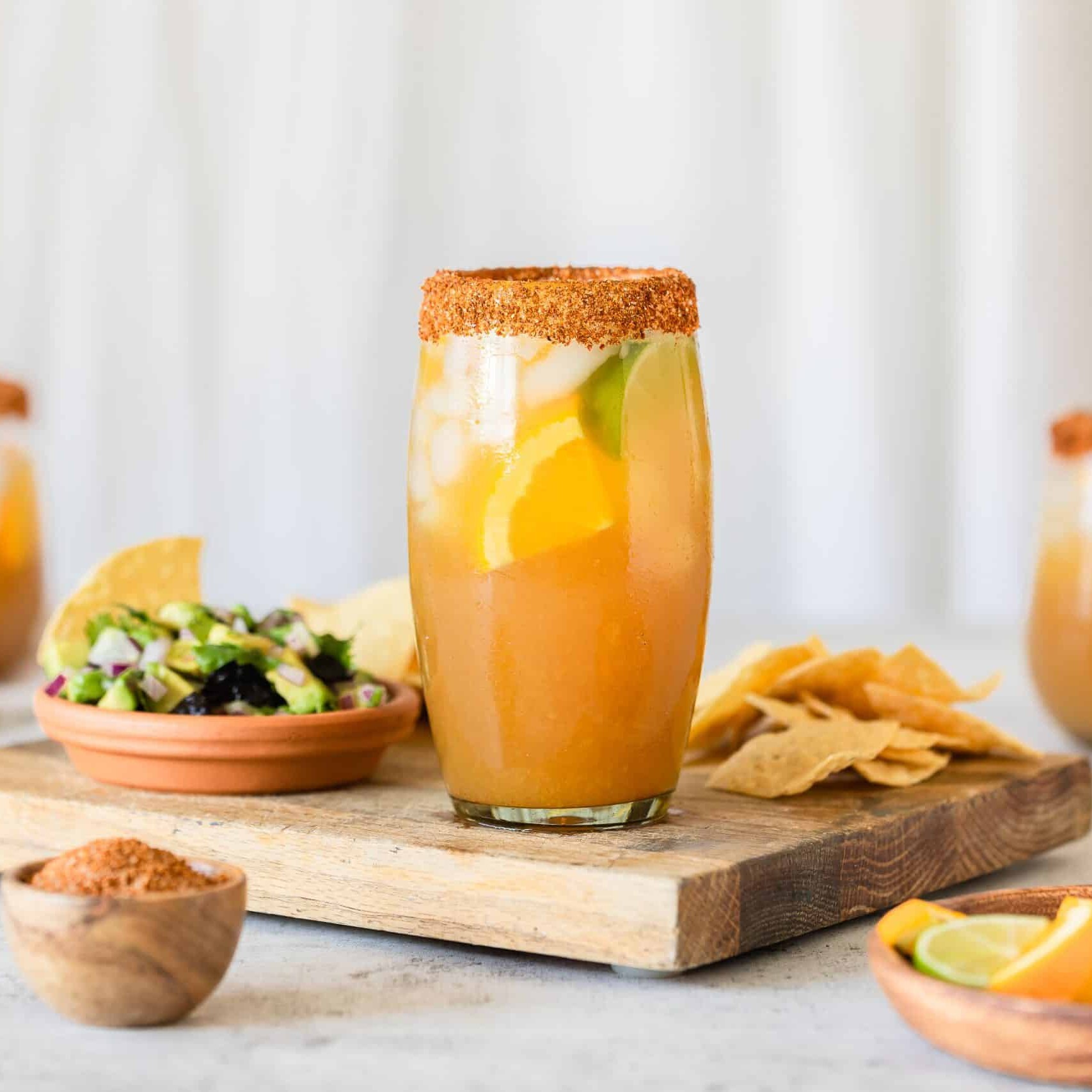 a glass filled with a California Prune and Fresh Orange Margarita on a cutting board with chips and salsa