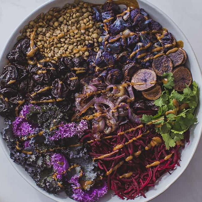 Spiced Purple Power Bowl with a cup of dressing and two wooden spoons