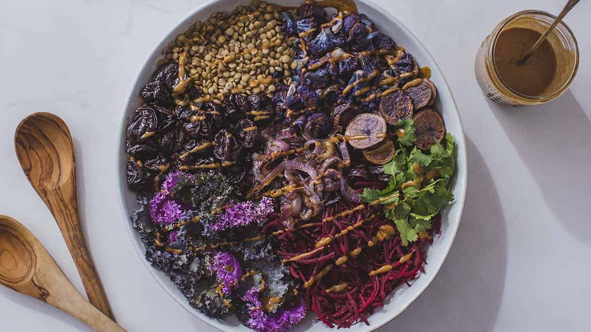 Spiced Purple Power Bowl with a cup of dressing and two wooden spoons
