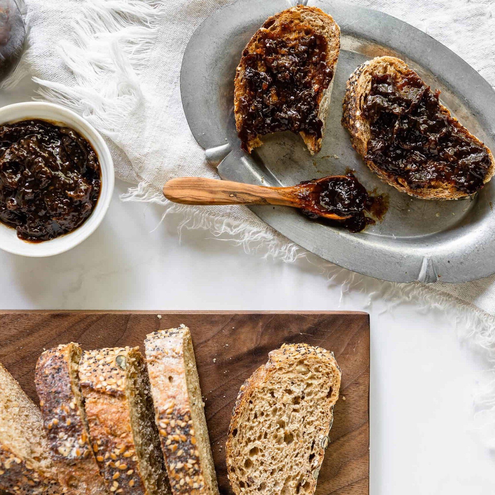 a bowl of Spiced California Prune Jam, both in a bowl and spread on to rustic slices of toast