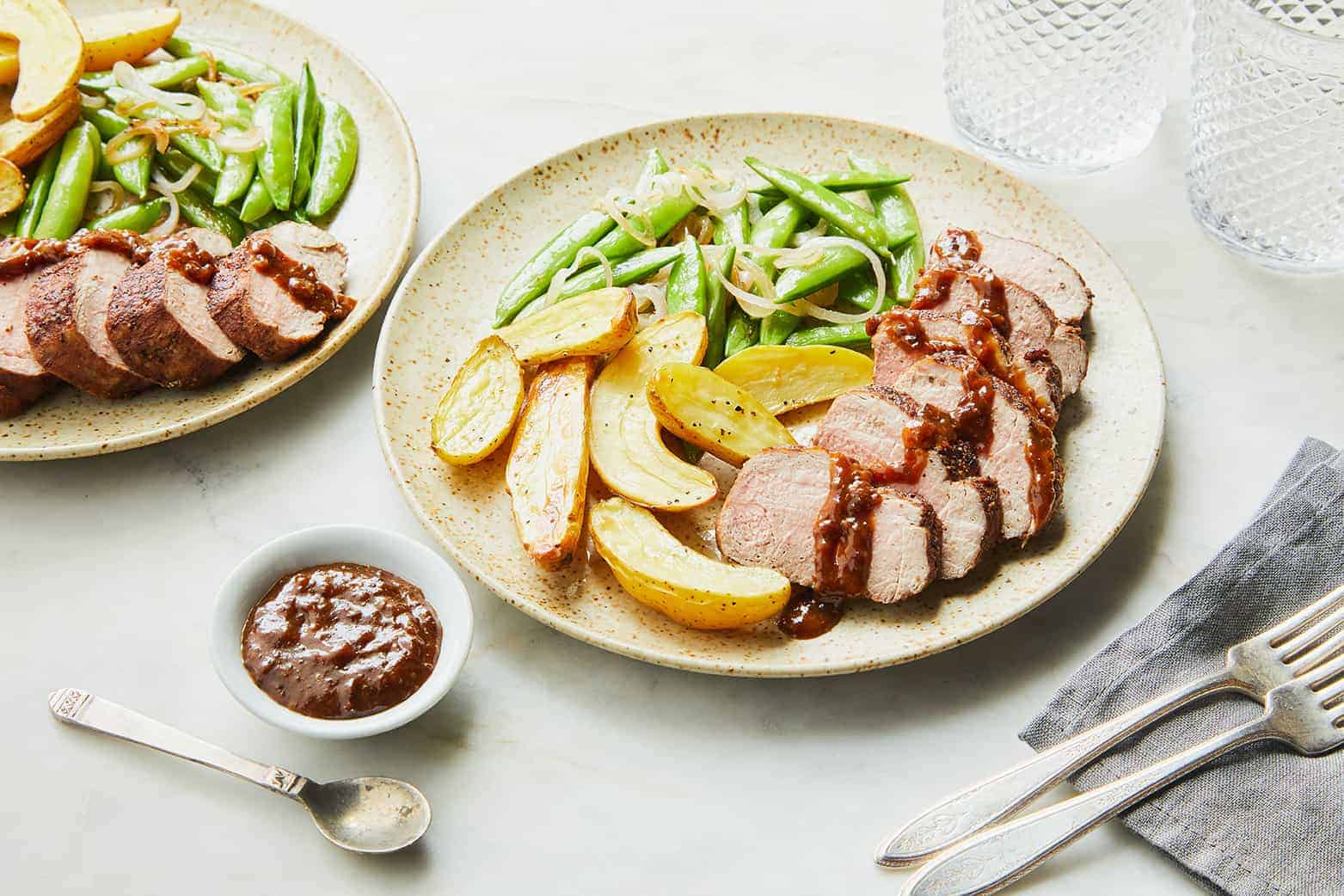 a plate filled with potatoes, prune-glazed pork tenderloin and snap peas