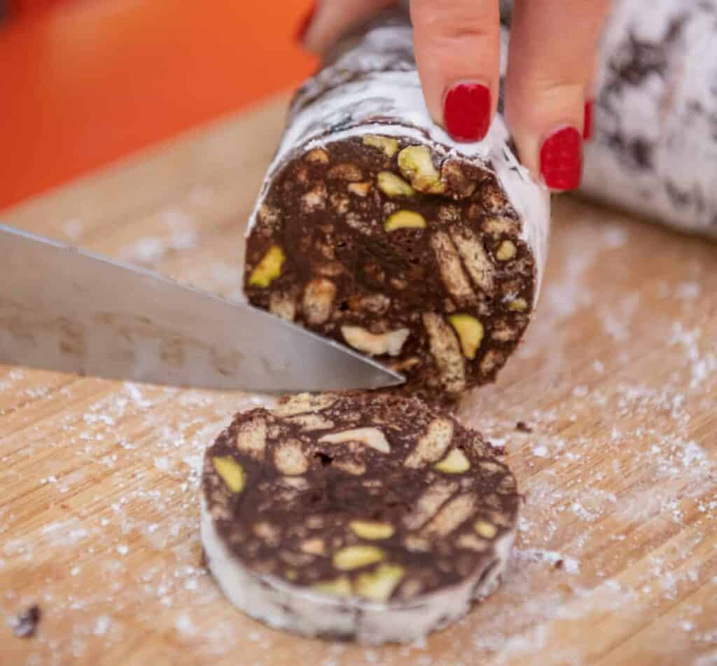 a knife slicing into a roll of chocolate salami