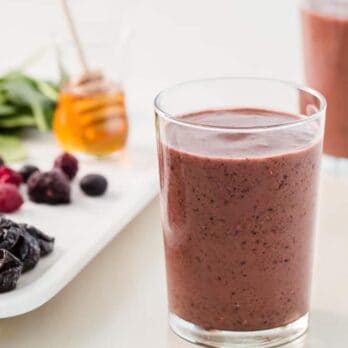two glasses of Purple Power Smoothies on a plate with berries and prunes