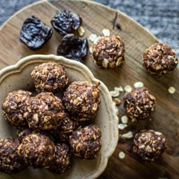 a bowl full of Chocolate Energy Balls surrounded by additional chocolate energy balls and prunes