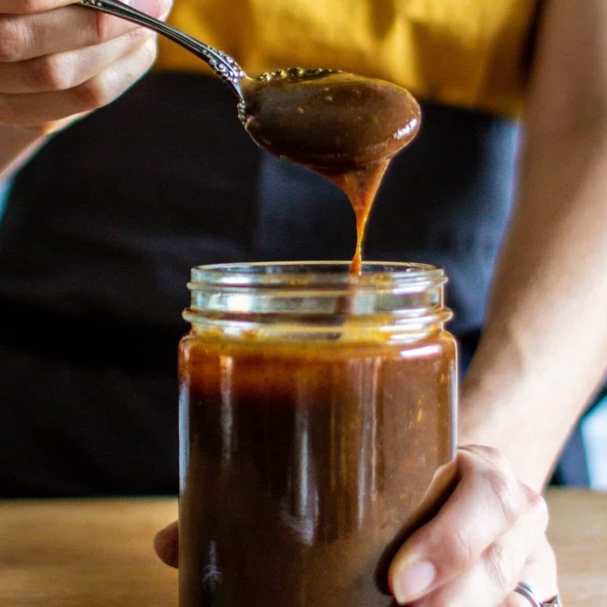 a woman pulling a spoon of prune puree out of a jar