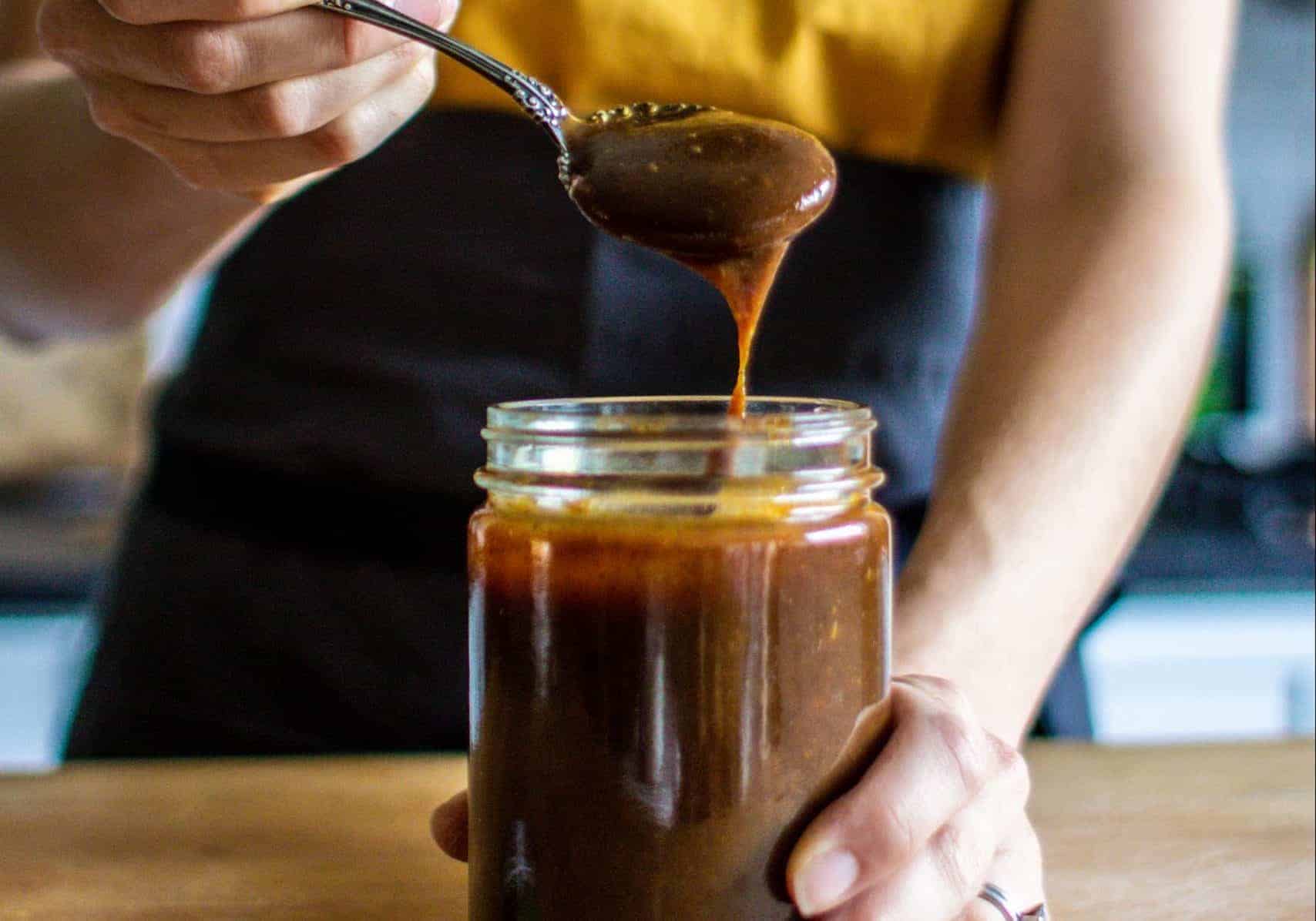 a woman pulling a spoon of prune puree out of a jar