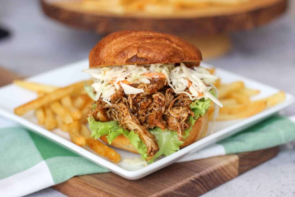 Pulled Chicken sandwiches topped with coleslaw on a plate with french fries