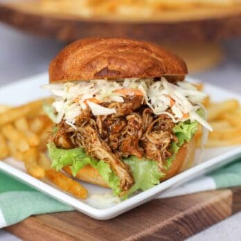 Pulled Chicken sandwiches topped with coleslaw on a plate with french fries