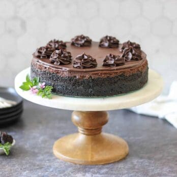 a cake plate topped with Double Chocolate Cheesecake and a stack of black plates
