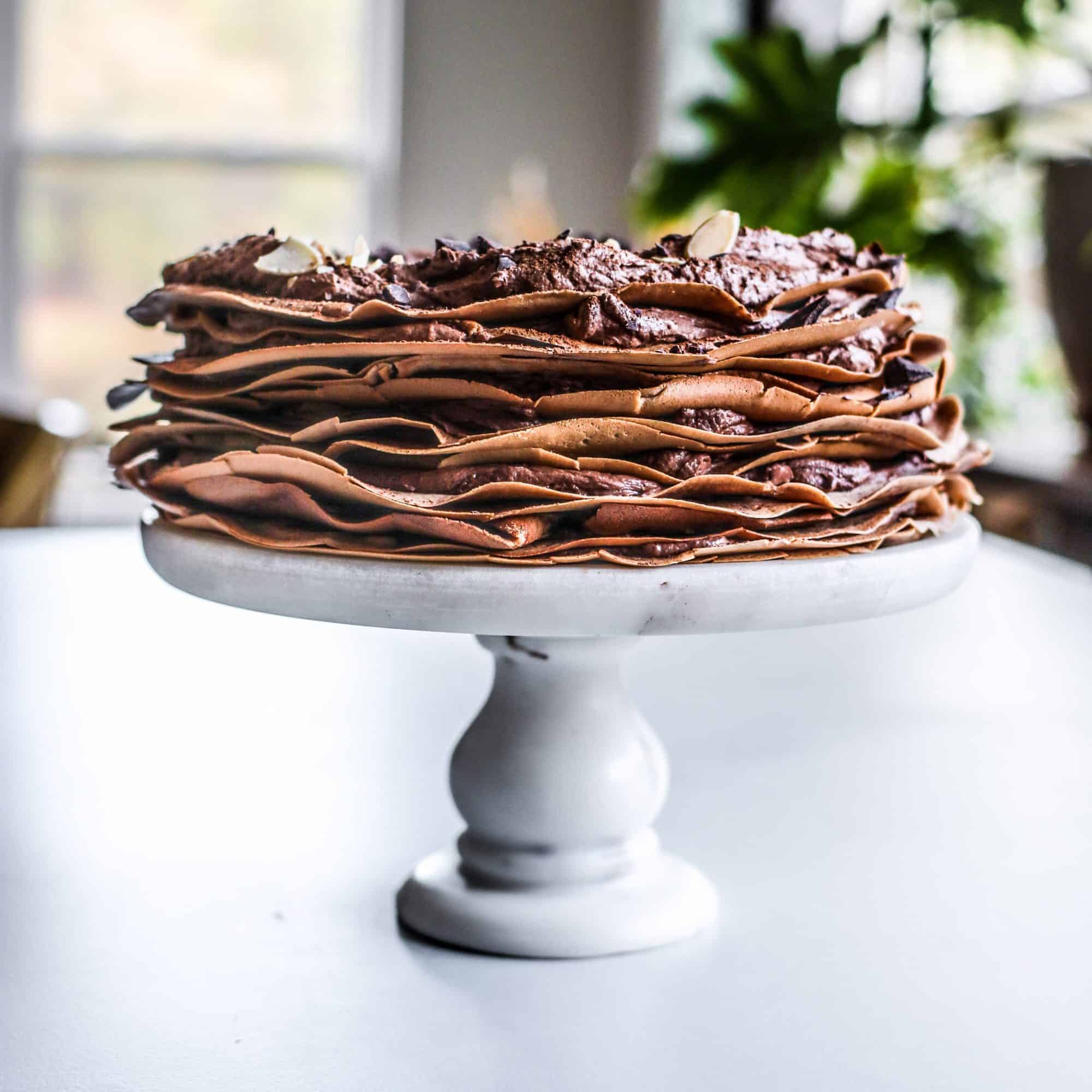 chocolate crepes layered to make a chocolate crepe cake are stacked on a cake plate