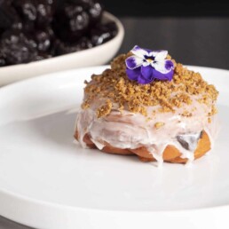a glazed Jelly Donut with California Prunes on a plate and topped with an edible flower