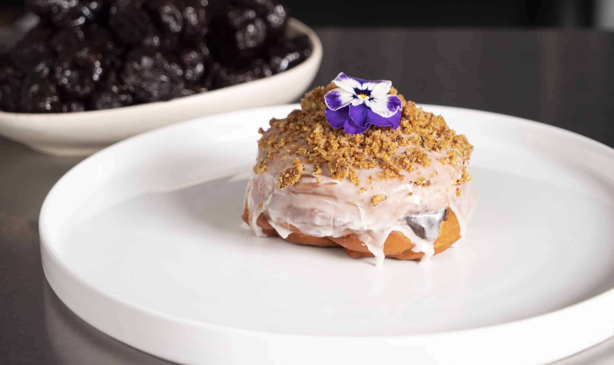 a glazed Jelly Donut with California Prunes on a plate and topped with an edible flower