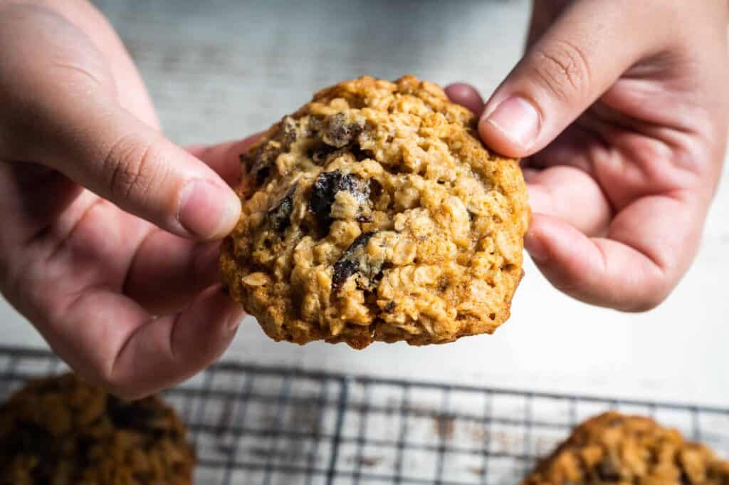 two hands snapping an old-fashioned chewy oatmeal cookie with chocolate