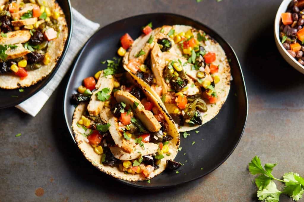 a black plate with 2 Chicken Tacos with California Prunes Salsa