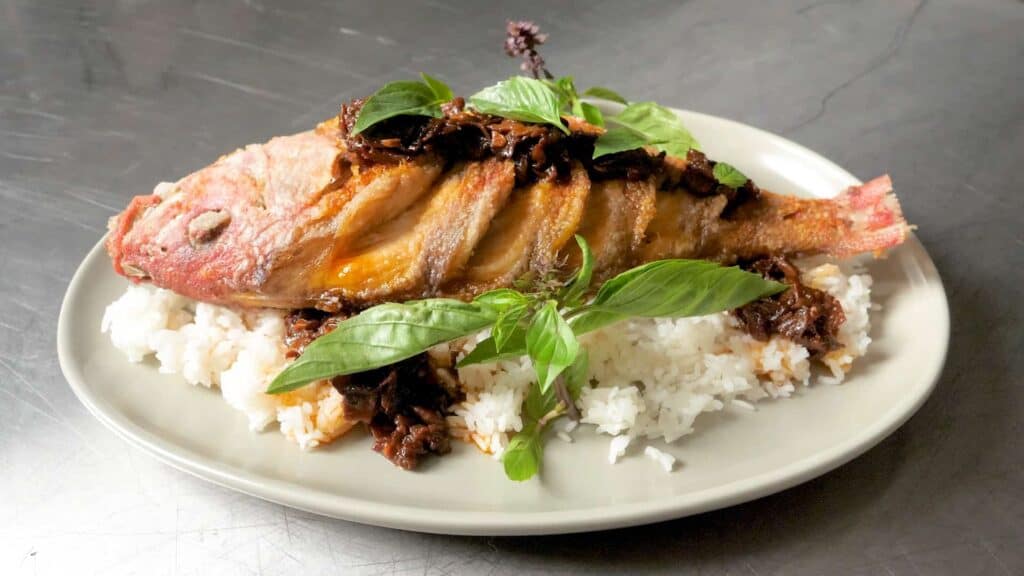a white plate with white rice, basil and Whole Fried Snapper With Prune XO Sauce