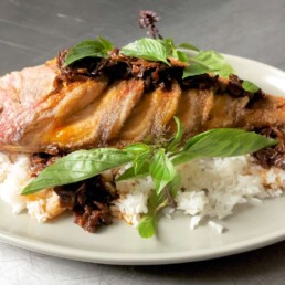 a white plate with white rice, basil and Whole Fried Snapper With Prune XO Sauce