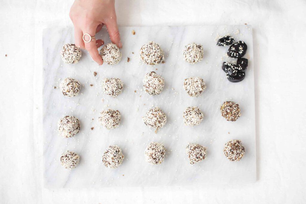 a hand reaching for Sesame Seed California Prune Balls on a piece of parchment paper