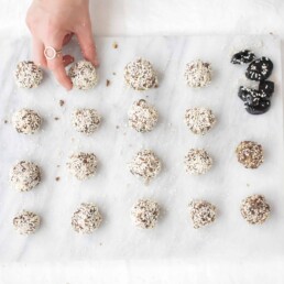 a hand reaching for Sesame Seed California Prune Balls on a piece of parchment paper