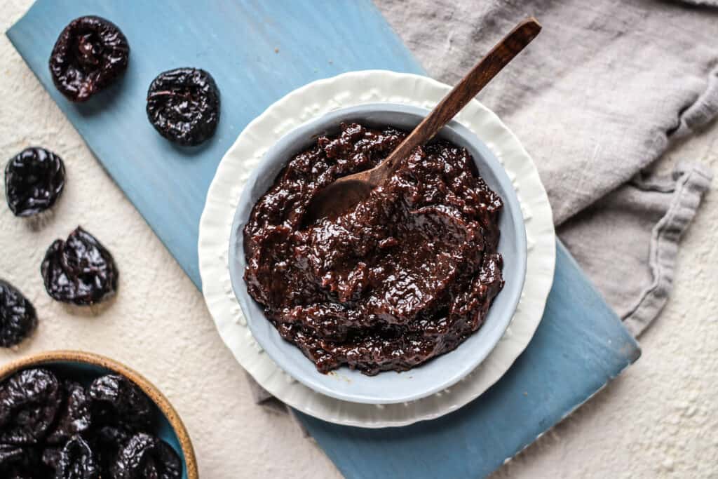 a bowl of prune puree with a spoon in it with a bowl of prunes
