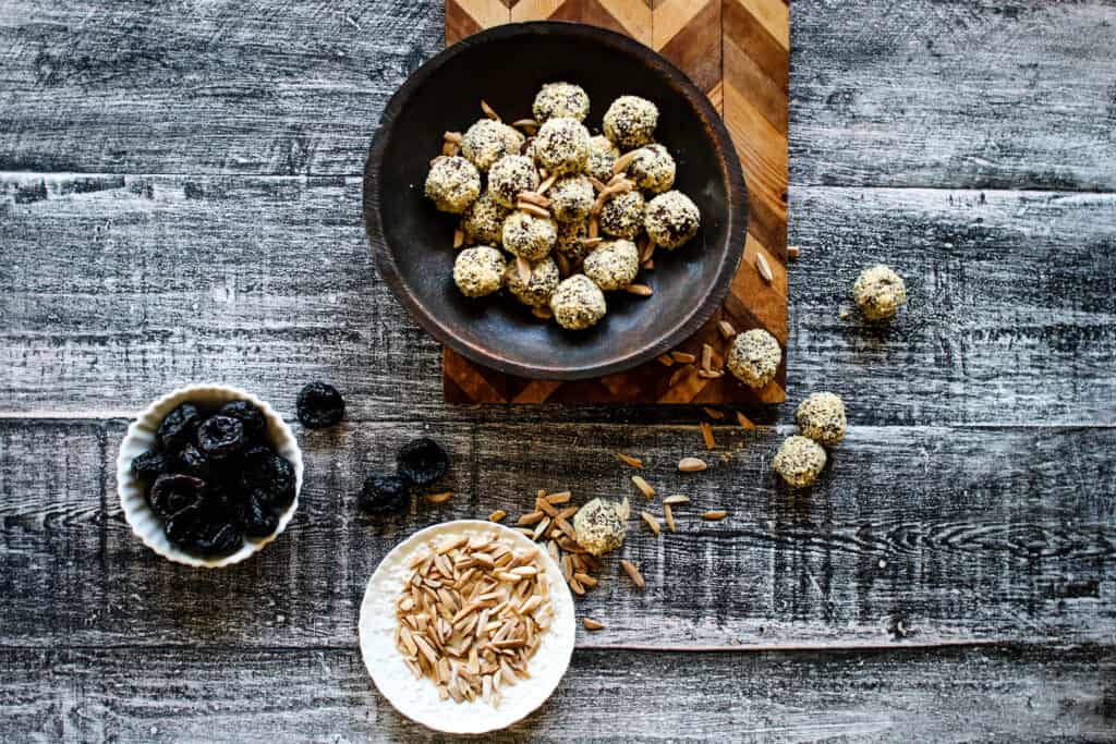 California a bowl of Prune & Almond Truffles on a cutting board with a bowl of prunes and sliced almonds