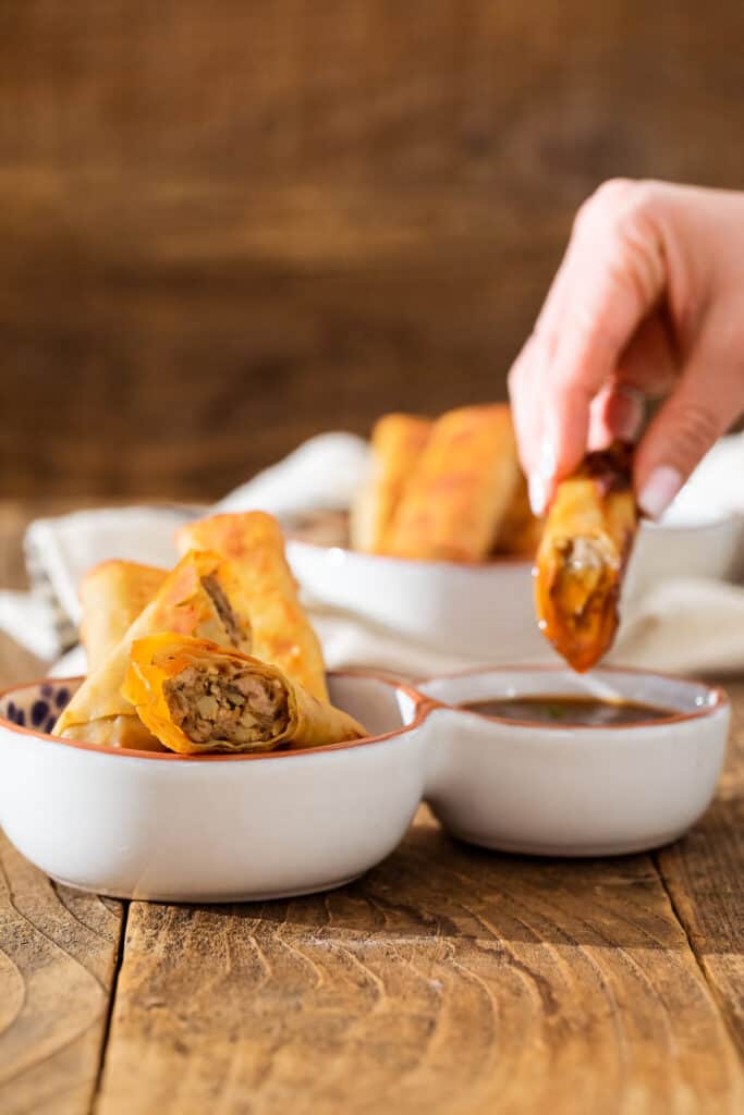 a hand dipping lumpia into prune purée dipping sauce