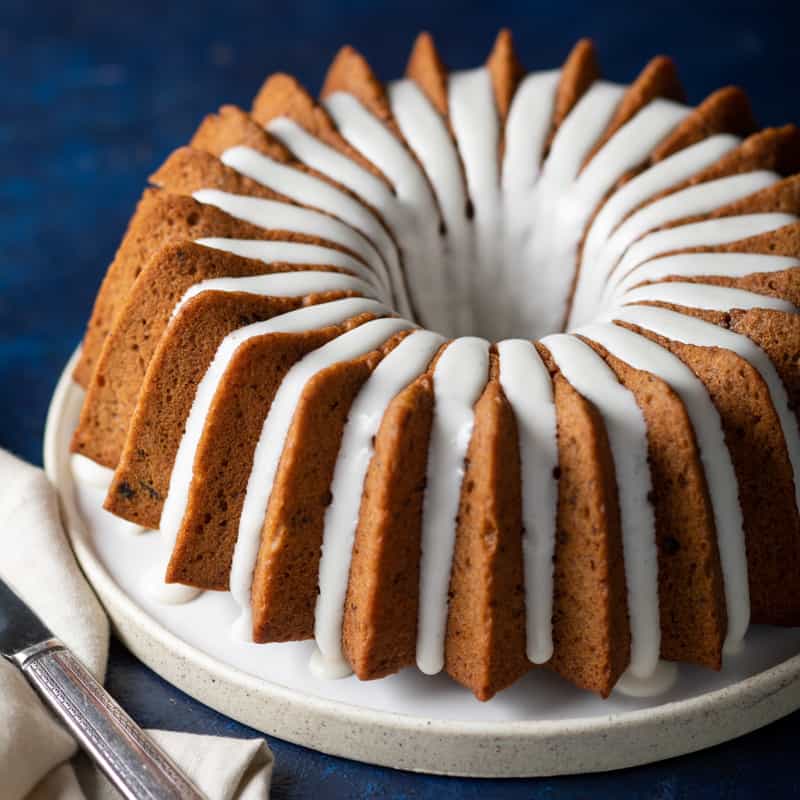 a cake plate with a geometric banana prune bundt cake and icing from bake from scratch