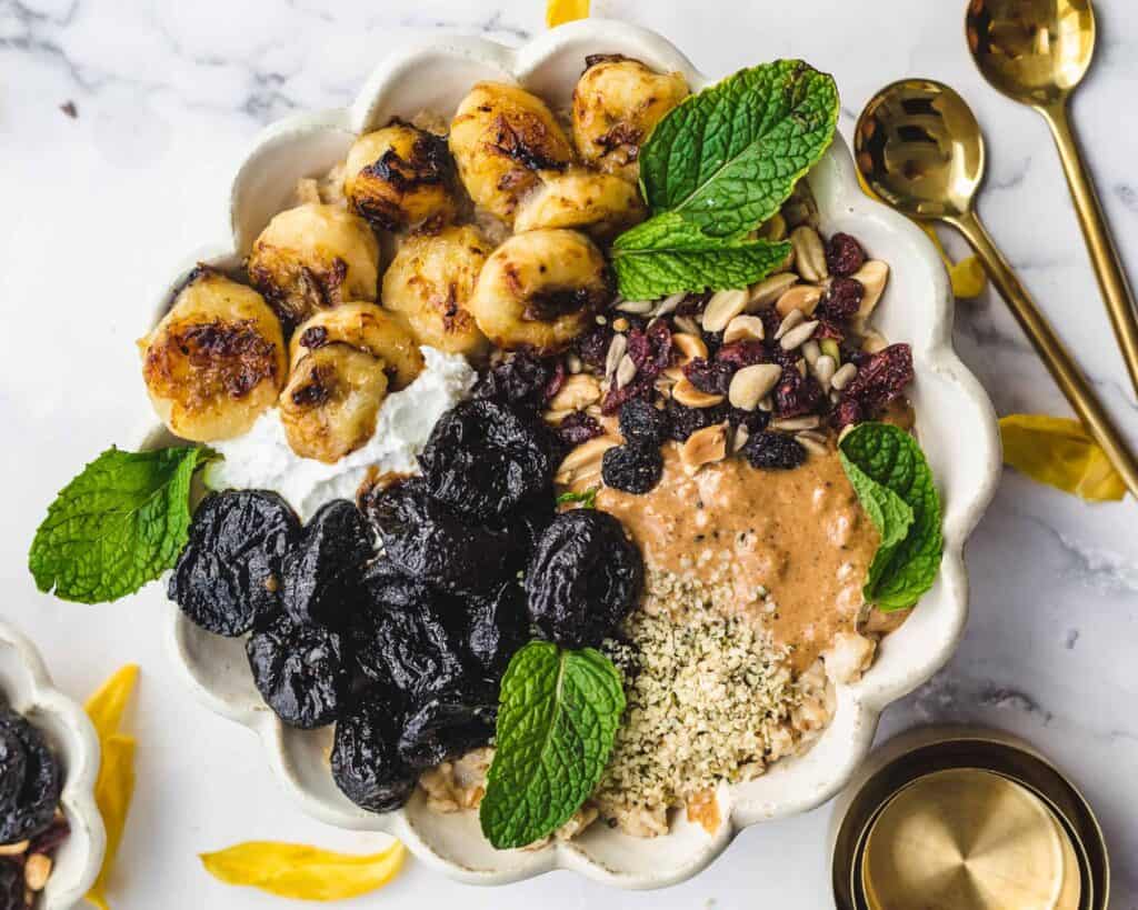a scalloped bowl filled with caramelized banana, prunes, yogurt and peanut butter drizzle