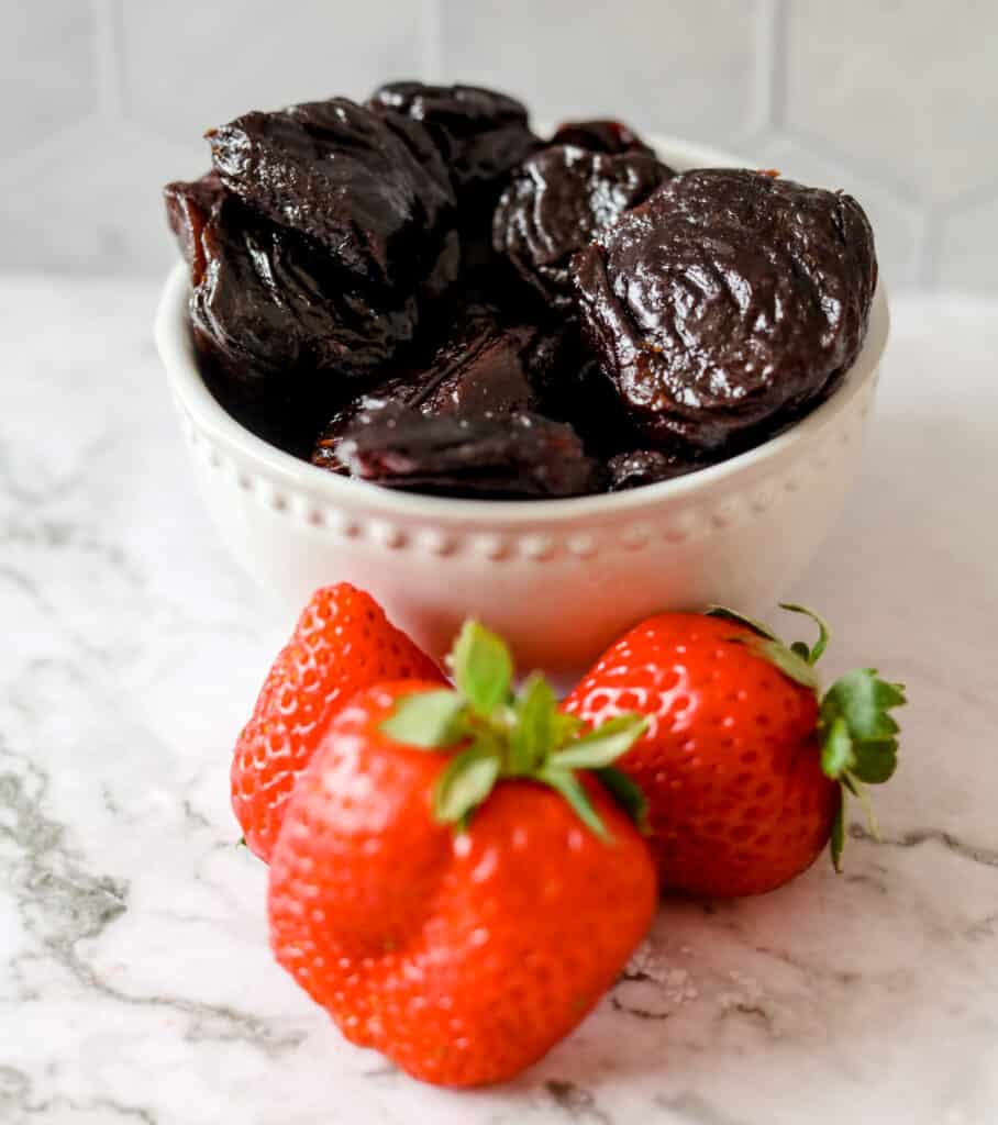 a bowl with prunes next to strawberries