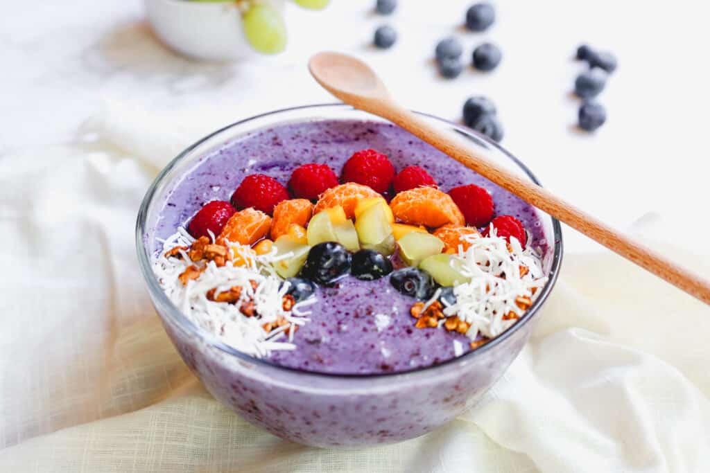 Eat the Rainbow Smoothie for California Dairy ebook - a purple bowl with yogurt, blueberries, blue spirulina, prunes, chia seeds, raspberries, mango, tangerines, grapes, granola, coconut 