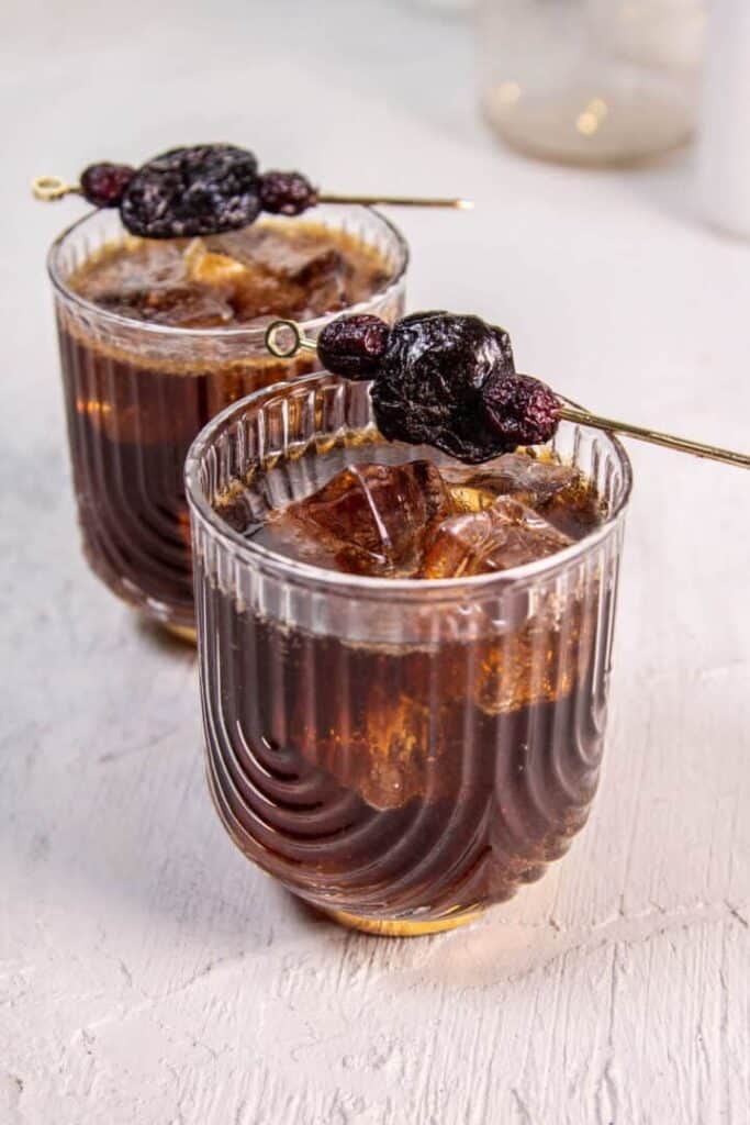 Two Fruitcake Rum and Coke cocktails from This Mess is Ours with skewered prune garnish