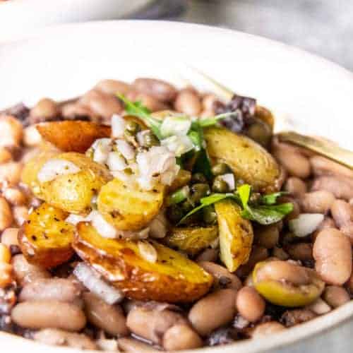 California Grown's recipe for Beans Marbella in a white bowl topped with roasted potatoes