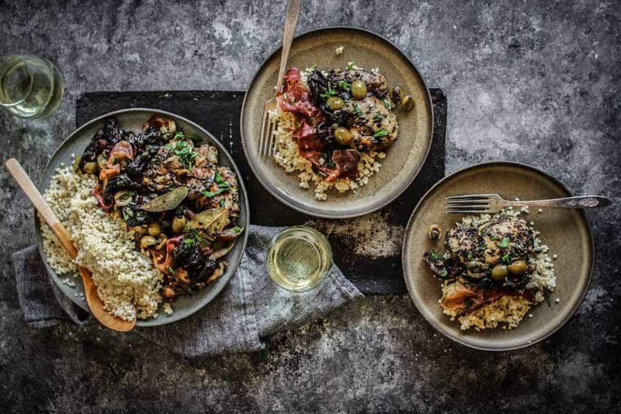 Three plates of Sheet pan Chicken Marbella from This Mess is Ours with two glasses of white wine