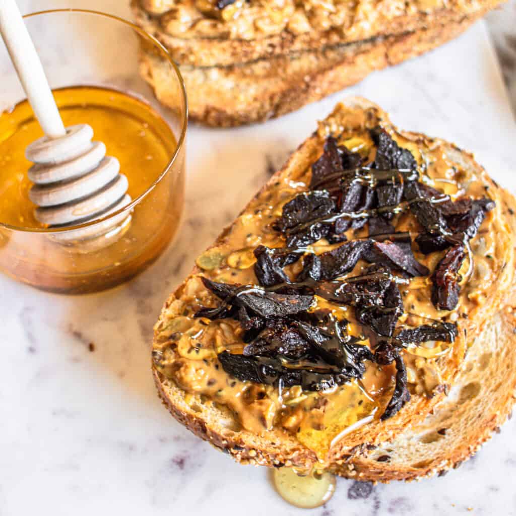 a piece of bread topped with peanut butter, prunes and honey