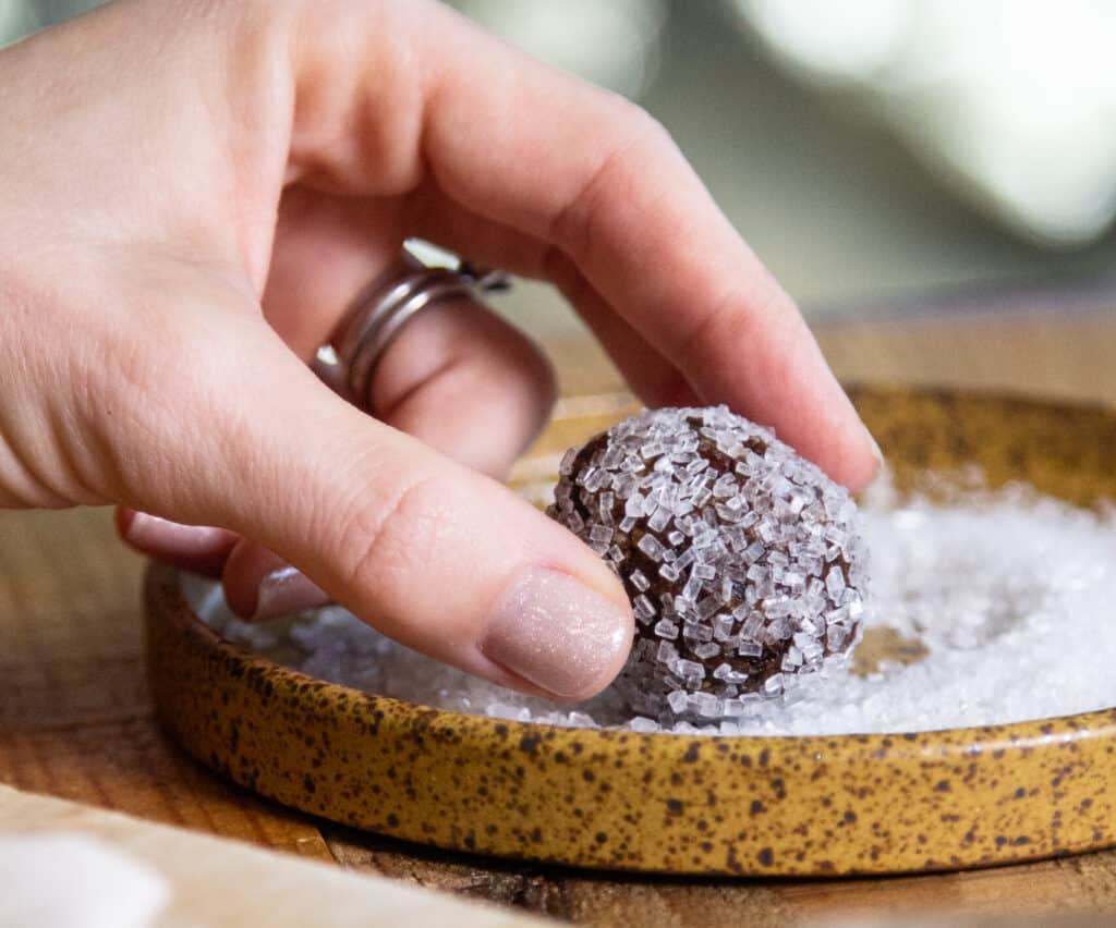 a hand rolling traditional sugar plum candy in sugar