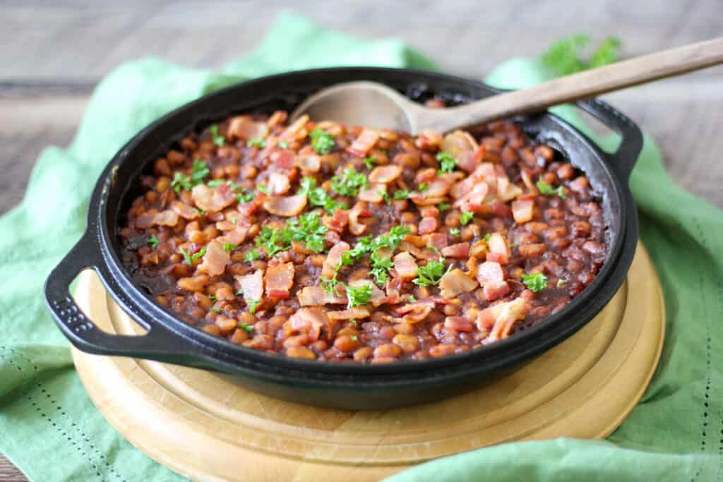 a cast iron skillet with a batch of naturally sweetened baked beans with a wooden spoon on top