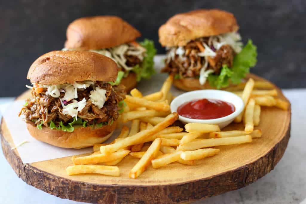Three BBQ pulled chicken sandwiches made using slow cooker pulled chicken recipe with french fries and ketchup