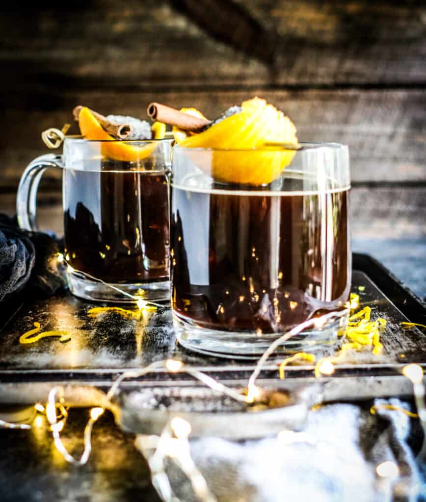two glass mugs of Warm Sugar Plum Cocktails garnished with citrus and cinnamon