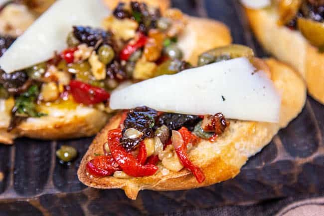a plate of bruschetta topped with prunes, nuts, sundried tomatoes and cheese