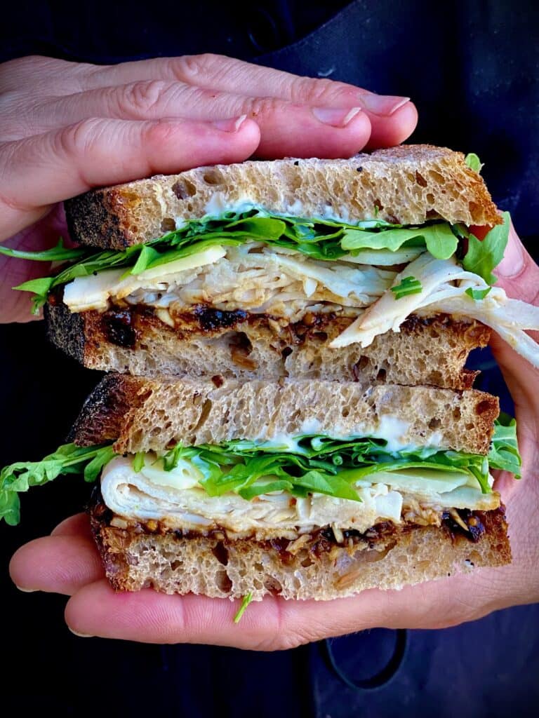 hands holding two halves of a Turkey Sandwich with Prune Mostarda