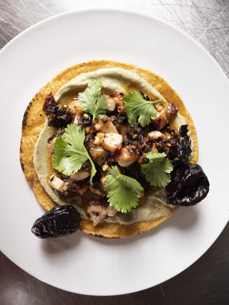Tostada topped with Octopus, cilantro and Salsa Macha with prunes