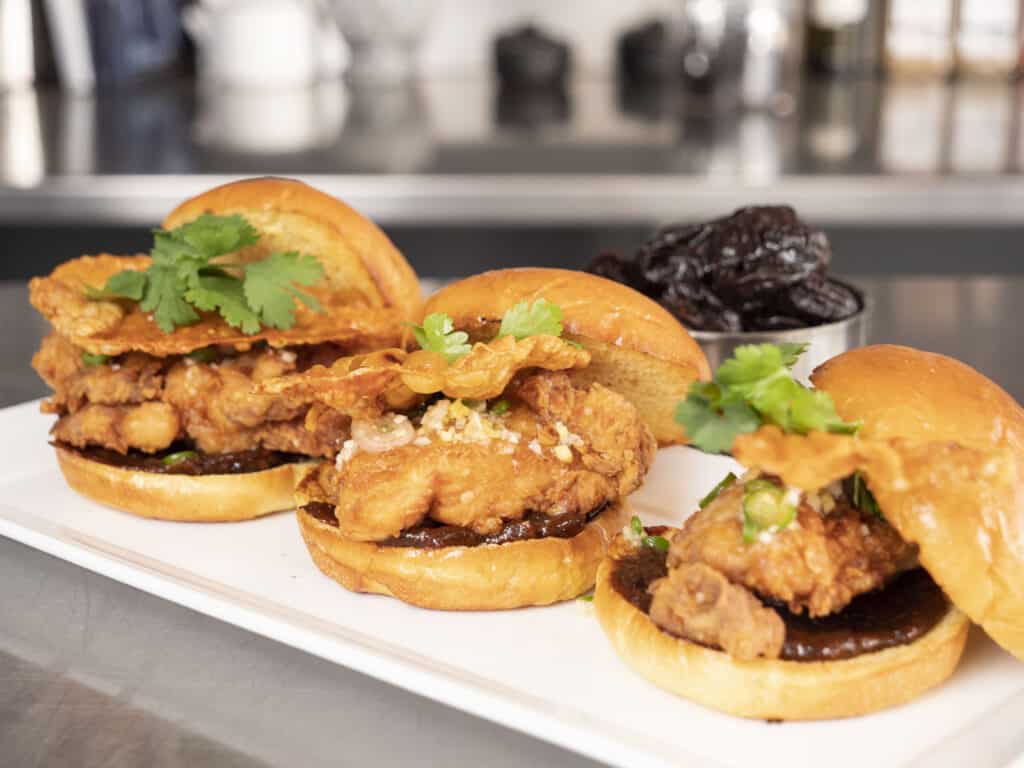 three fried chicken sandwiches lined up on a kitchen counter