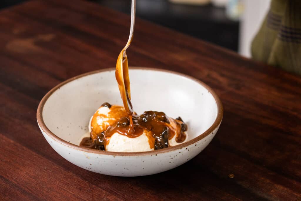 drizzling spiced prune caramel sauce onto a bowl of ice cream