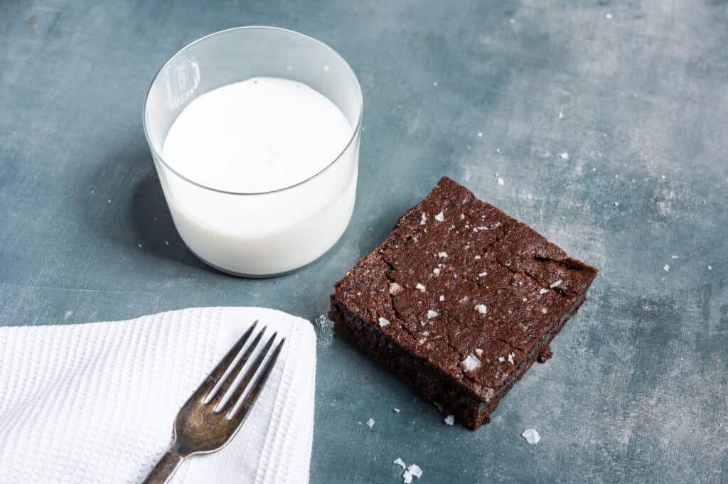 a slice of vegan brownies with a glass of milk and a fork