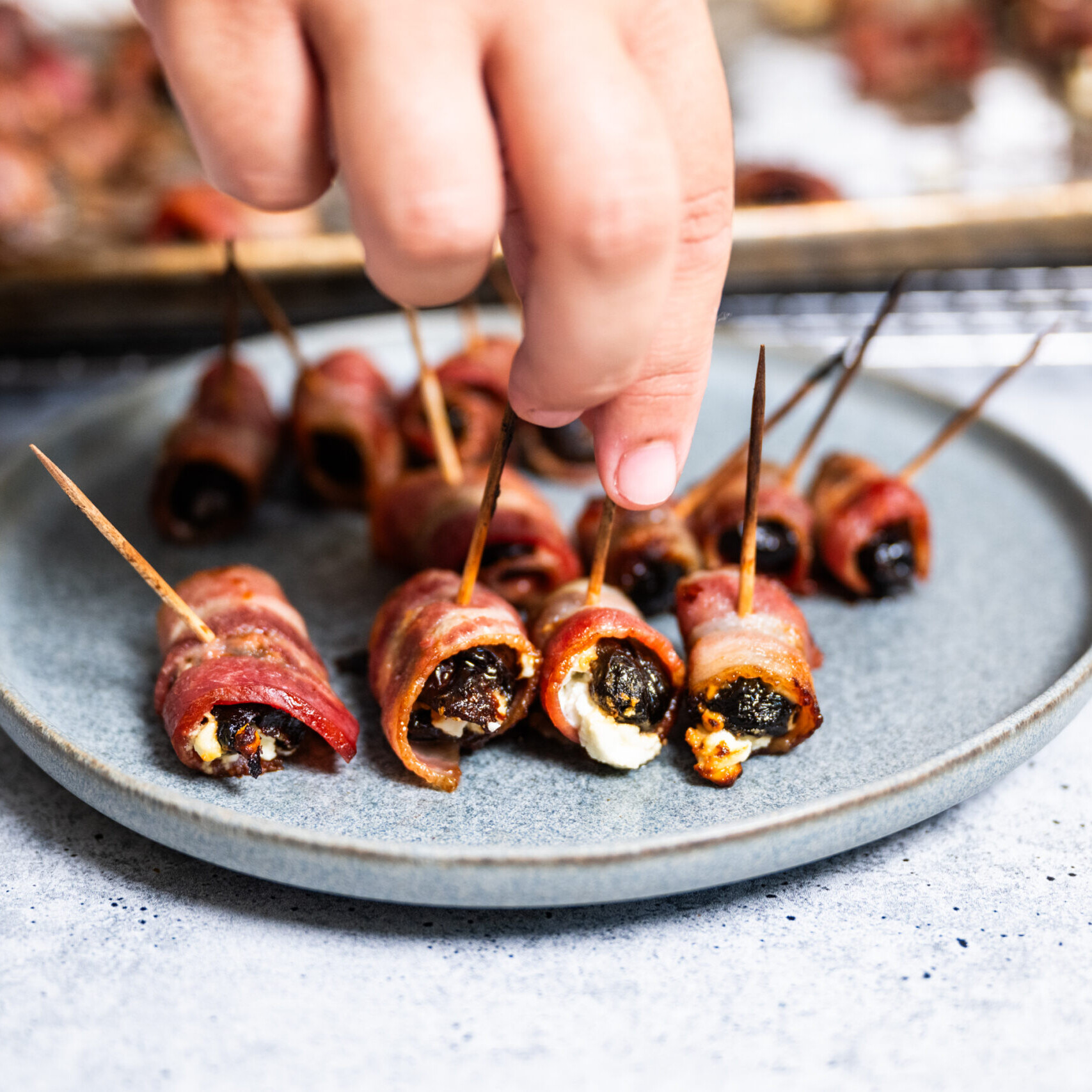 Devils on Horseback - Prunes stuffed with Goat cheese and wrapped in bacon Hand reaching to grab a bacon wrapped prune
