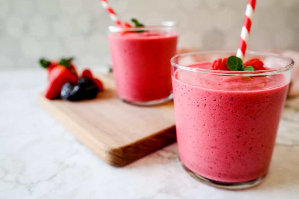Super Pink Smoothie in a glass topped with raspberries with a striped straw