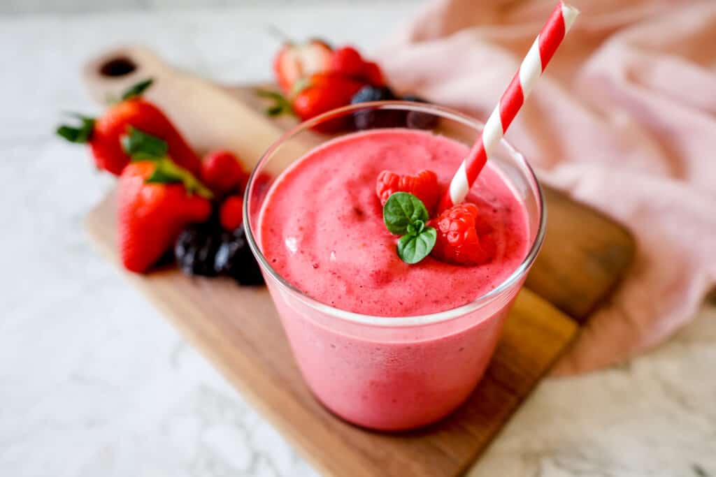 a glass of Super Pink Smoothie garnished with raspberries and a straw