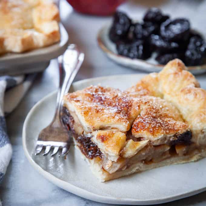 a slice of apple, prune and brandy slab pie on a plate with a fork